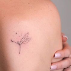 a woman's back shoulder with a small dragonfly tattoo on it