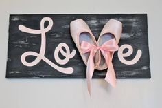 a pair of pink ballet shoes hanging on a sign with the word love painted on it