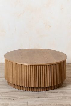 a round wooden table sitting on top of a hard wood floor next to a wall