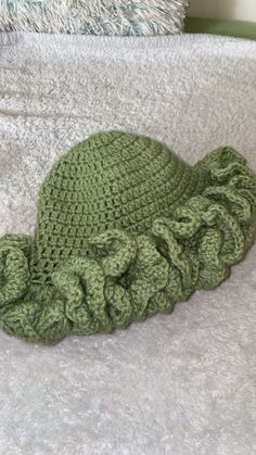 a green crocheted hat laying on top of a white bed cover with ruffles