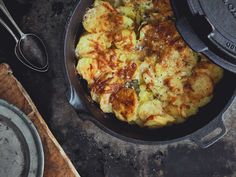 a skillet with some food inside of it on a wooden table next to utensils