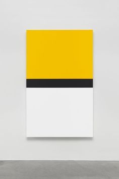 a yellow and white painting hanging on the side of a wall in an empty room