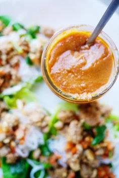 a glass jar filled with sauce sitting on top of a white plate next to lettuce