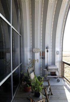 a balcony with chairs and potted plants on the outside wall, overlooking an open field