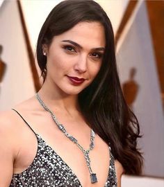 a woman with long dark hair wearing a silver dress and holding a necklace on her neck