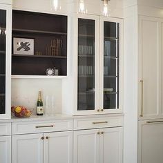 a kitchen with white cabinets and black glass front doors, wine glasses on the counter