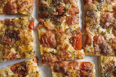 several square pieces of pizza with tomatoes and herbs on them sitting on a white surface