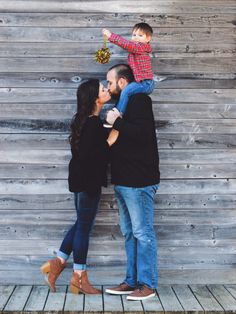 a man and woman are holding a small child in front of a wooden wall with planks