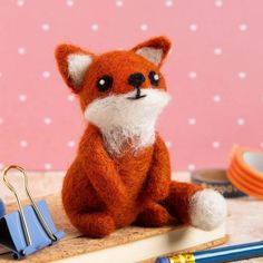 a stuffed fox sitting on top of a table next to a pen and paper clip