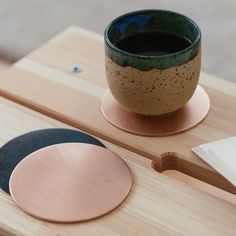 a coffee cup sitting on top of a wooden table next to a metal disc and paper