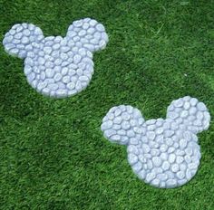 two mickey mouse heads made out of pebbles sitting on the grass in front of each other