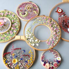 four embroidery hoops with flowers and birds in them on a gray surface, each decorated with different colored thread