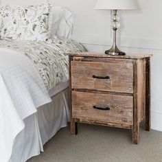 an old wooden nightstand next to a bed in a room with white sheets and pillows