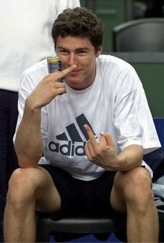 a tennis player sitting on the sidelines with his finger in his mouth while holding a drink