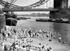 an old black and white photo of people on the beach in front of a bridge