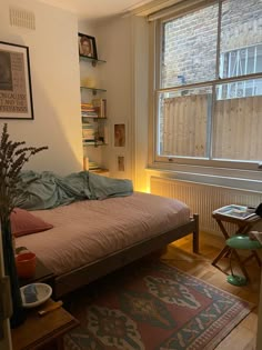 a bed sitting next to a window in a room with a rug on the floor