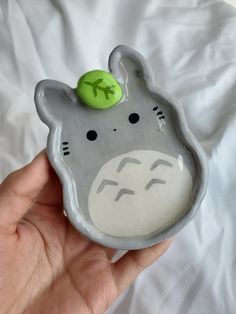 a hand holding a gray and white ceramic animal with a green ball on it's head