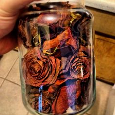 a hand holding a glass jar filled with dried red and orange roses on the counter