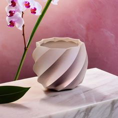 a white vase sitting on top of a table next to a purple wall with flowers in it