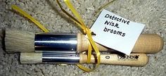 two wooden brushes are wrapped in yellow ribbon and labeled with a note that says, detative nisk brooms