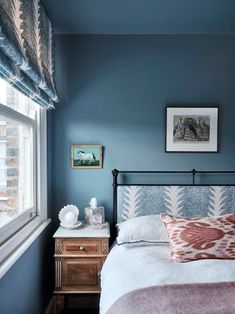 a bed sitting next to a window in a room with blue walls and wooden floors