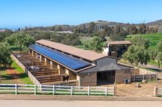 an aerial view of a barn with solar panels on it's roof and horses in the background