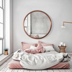 a bedroom with a round mirror above the bed and pink pillows on the bottom floor