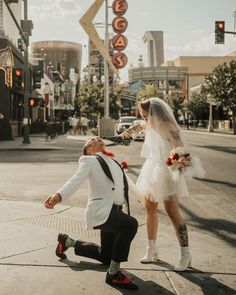 a man kneeling down next to a woman in a white dress and tuxedo