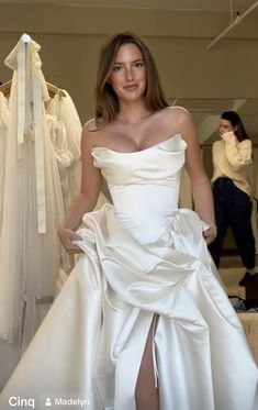 a woman in a white dress standing next to some wedding gowns