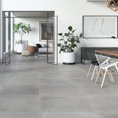 a room with white walls and grey flooring has plants on the tables in it