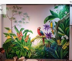 a man sitting at a table in front of a mural with birds and tropical plants