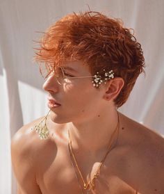 a shirtless young man with red hair and flowers in his hair, wearing glasses