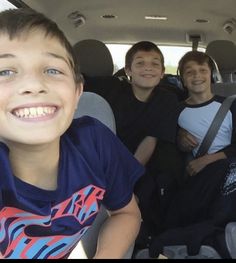 three boys are sitting in the back seat of a car and one boy is smiling