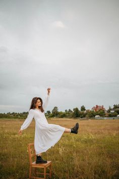 a woman in a white dress is sitting on a wooden chair and flying a kite