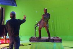 two men are standing in front of a green screen and one is holding his hand out