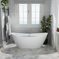 a white bath tub sitting in a bathroom next to a window with potted plants