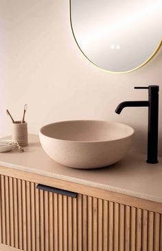 a white bowl sink sitting on top of a wooden counter next to a round mirror