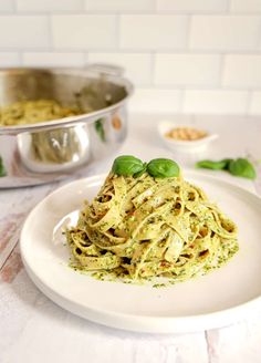 a white plate topped with pasta covered in pesto sauce and garnished with green leaves