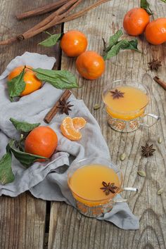 two glasses filled with orange juice on top of a wooden table next to cinnamon sticks