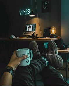 a person holding a coffee mug in their lap while sitting at a desk with a laptop