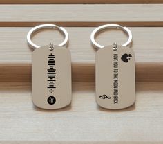 two metal key chains sitting on top of a wooden table next to each other with writing on them