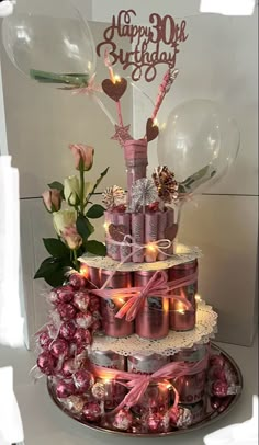 a three tiered birthday cake with balloons and decorations on the top, surrounded by pink candies