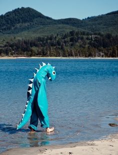 a blue dragon is standing in the water at the edge of a lake with mountains in the background