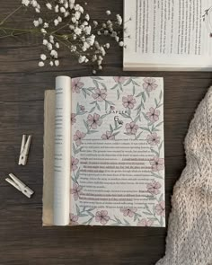 an open book sitting on top of a wooden table next to a plant and pen