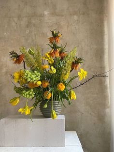 a vase filled with yellow and orange flowers on top of a white table next to a window