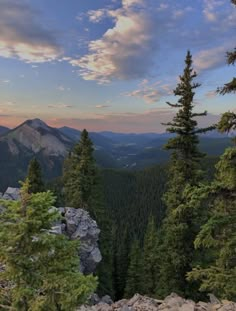 the sun is setting in the mountains with pine trees and rocks on the ground below