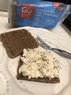 there is a sandwich on a white plate with a fork and bag of bread in the background