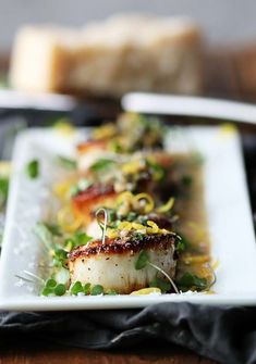 a white plate topped with scallops covered in sauce and garnished with green onions