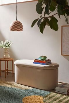 a living room with a plant and some books on the ottoman next to a potted plant