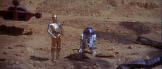 star wars action figures in the desert with one robot standing next to the other figure